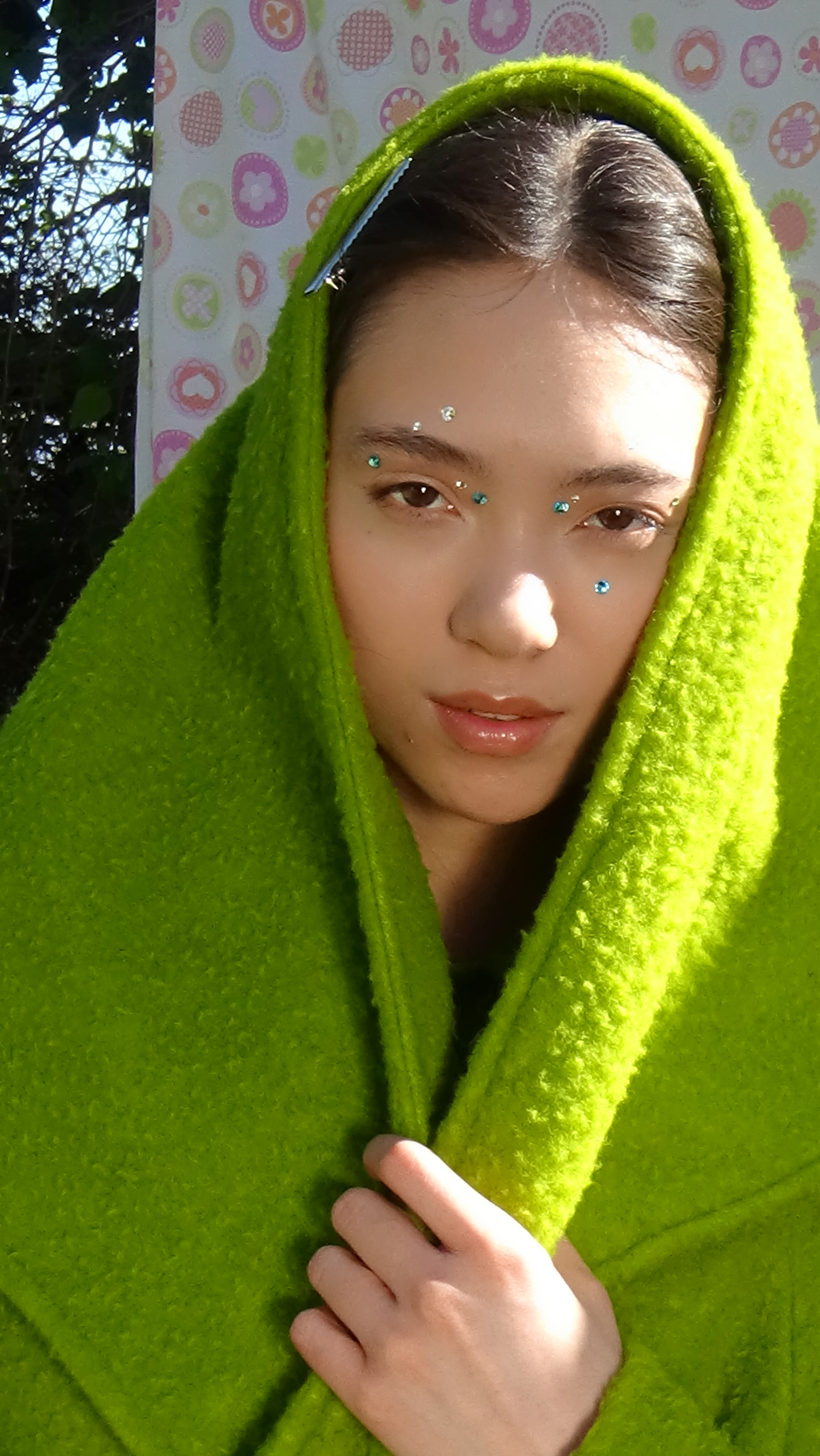 Close up portrait of a female model in a green head scarf with radiant skin and blue and white gems around her eyes.